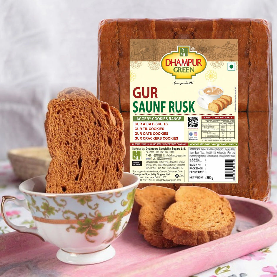 Packaging of Gur Saunf Rusk showing the product name and Rusks placed beside a cup of tea and on a plate, indicating the product is meant to be enjoyed with tea.